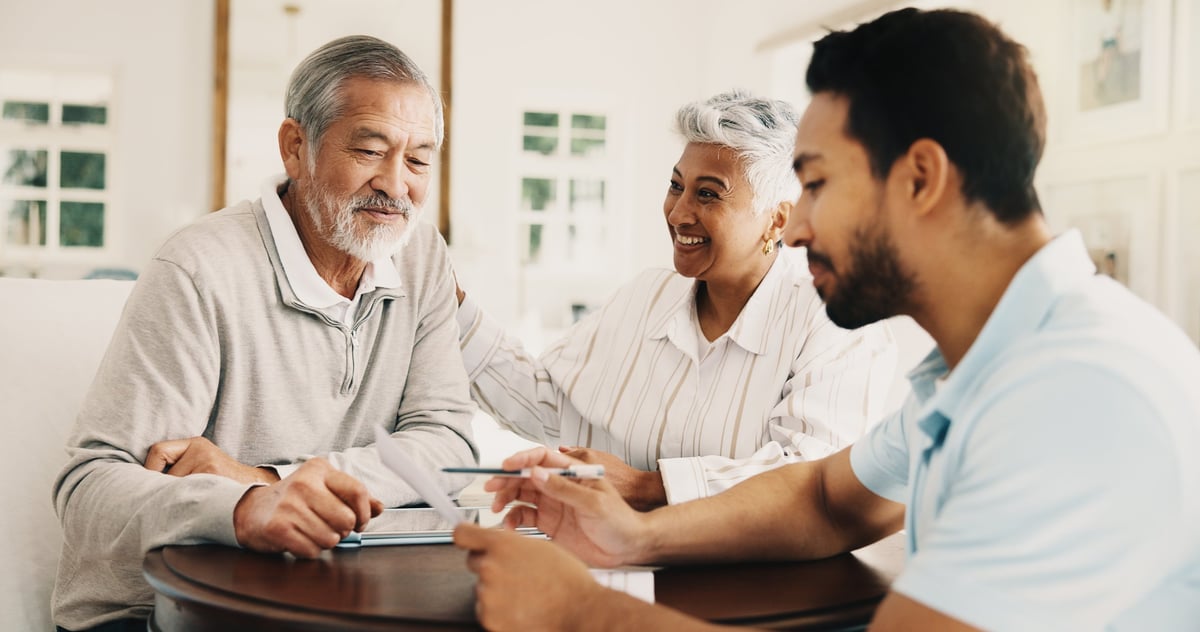 Pareja de adultos mayores sonriendo mientras un asesor financiero revisa con ellos sus documentos y ahorro para el retiro